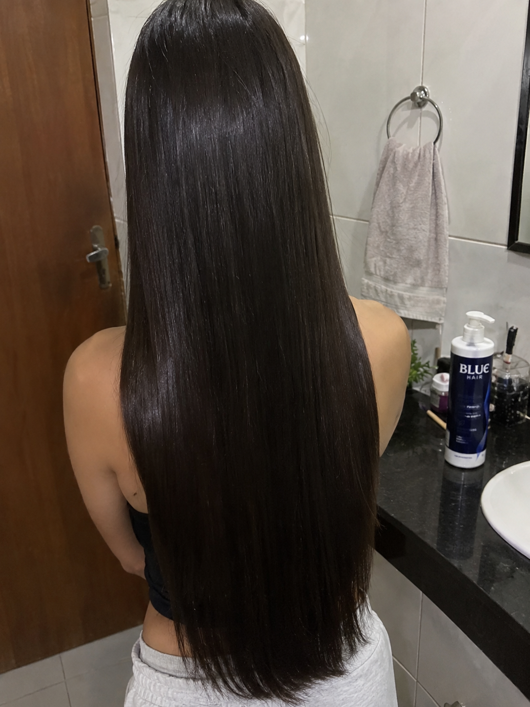 Fotografia de cabelo longo visto de costas, com frasco BLUE Hair ao fundo